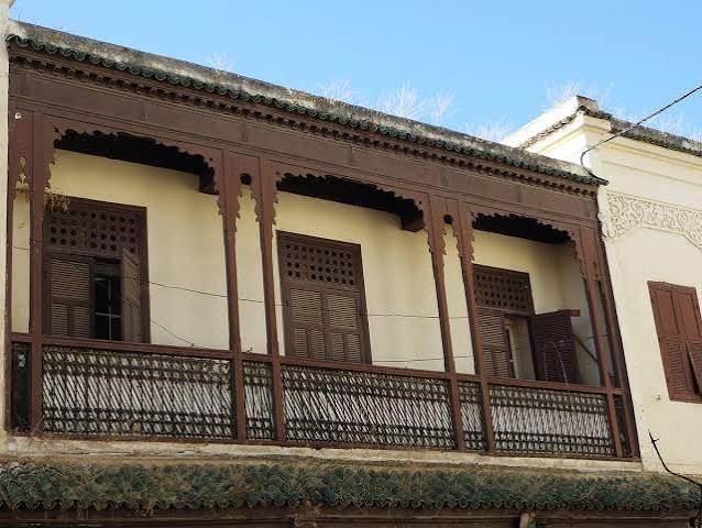 The characteristic wooden balconies of a Moroccan Mellah — carved, projecting over the street, their dark-painted fretwork the most distinctive architectural signature of the historic Jewish quarter and the detail that immediately distinguishes the Mellah from the surrounding Muslim medina